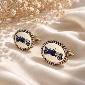 May include: A pair of oval-shaped cufflinks featuring a gold-toned metal finish with a braided border. The center of each cufflink displays a detailed illustration of a vintage blue and white open-top car with black wheels and a steering wheel.