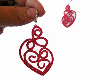 May include: A pair of red heart-shaped earrings made of crocheted thread. The earrings are delicate and intricate, with a swirling pattern.