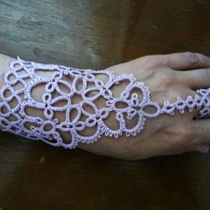 May include: A delicate lavender lace bracelet with a finger loop. The bracelet is made of intricate crocheted patterns and is designed to fit snugly around the wrist.