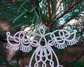 Può includere: Ciondolo a forma di angelo in pizzo bianco appeso a un ramo di pino. L'angelo presenta dettagli intricati e un design delicato.