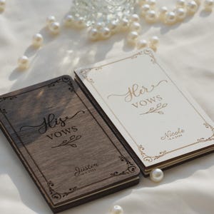 Op de afbeelding: Twee rechthoekige gelofteboekjes met houten kaften. Het linkerboekje is van donkerbruin hout met de tekst 'His VOWS' en 'Justin 10.4.2024'. Het rechterboekje is van licht crèmekleurig hout met 'Her VOWS' en 'Nicole 10.4.2024'. Beide hebben sierlijke randen.