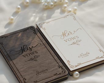Puede incluir: Dos libros de votos rectangulares con cubiertas de madera. El libro izquierdo es de madera marrón oscura con el texto 'His VOWS' y 'Justin 10.4.2024'. El derecho es de madera color crema claro con 'Her VOWS' y 'Nicole 10.4.2024'. Ambos tienen bordes ornamentados.