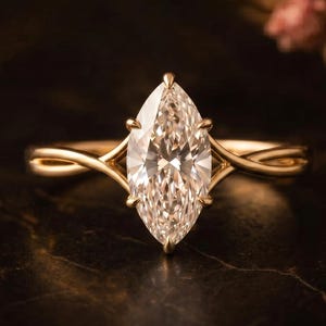 May include: A marquise-cut diamond engagement ring with a gold band. The diamond is the focal point, set in a four-prong setting. The band features a twisted design. The ring is displayed on a dark, textured surface.