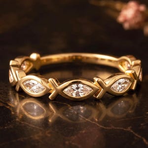 Puede incluir: Un anillo de banda dorada con un patrón repetitivo de piedras claras en talla marquesa que alternan con eslabones metálicos en forma de X. El anillo tiene un acabado pulido y un diseño continuo que rodea toda la circunferencia de la banda.