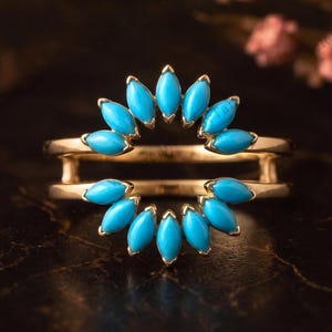 May include: A gold ring guard featuring two rows of marquise-cut turquoise stones arranged in a sunburst pattern. The ring has a double band design that frames a central space, with bright blue stones set in polished gold metal prongs.