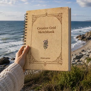 May include: A spiral-bound sketchbook with the text "Creative Grid Sketchbook" on the cover. The cover is a light brown colour with decorative corner designs and a small floral illustration. The name "Oliwia Jantar" is printed at the bottom.