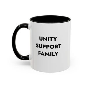 Op de afbeelding: Een witte keramische mok met een zwarte binnenkant en een zwart handvat. De buitenkant van de mok is voorzien van de tekst UNITY, SUPPORT, FAMILY, gedrukt in dikke, zwarte, schreefloze hoofdletters die verticaal in het midden staan.