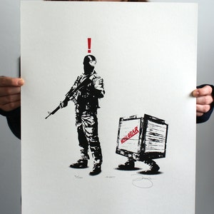 May include: A black and white illustration of a soldier holding a rifle, with a red exclamation point above his head. The soldier is standing in front of a wooden crate with the words "METAL GEAR" printed on it in red. The crate has legs and is walking. The image is signed "ALERT" and numbered "4/200".