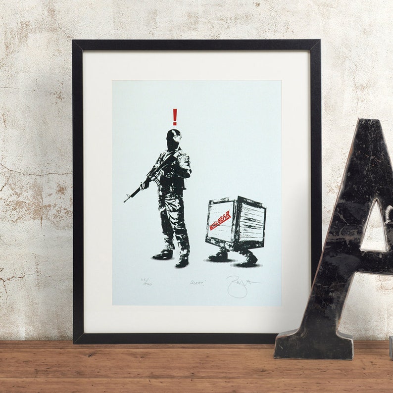 May include: A black and white print of a soldier holding a rifle with a box labeled "Solid Gear" walking behind him. The print is framed in a black frame.