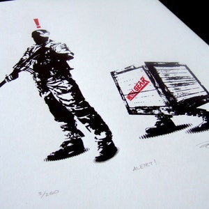 May include: Black and white illustration of a soldier holding a rifle, with an exclamation point above his head. A wooden box with the words "Metal Gear" printed on it is walking away from the soldier. The text "ALERT!" is printed below the box.