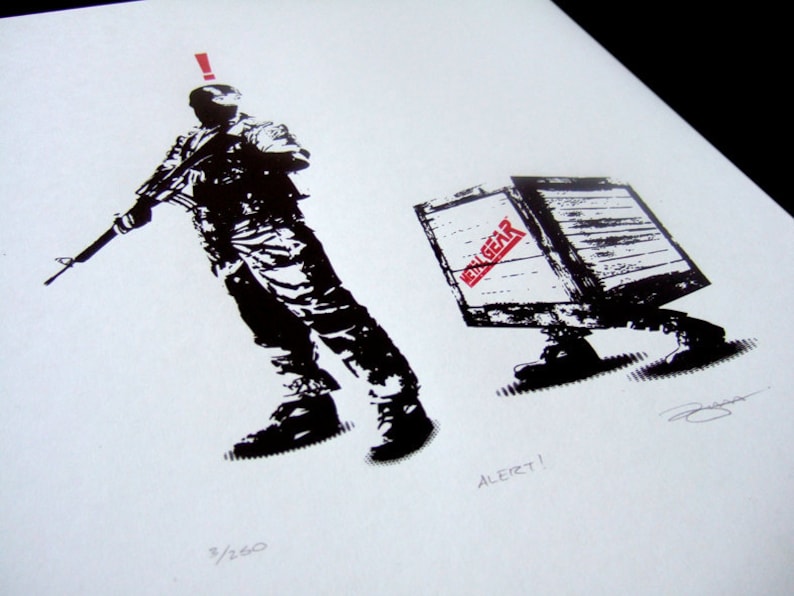 May include: Black and white illustration of a soldier holding a rifle, with an exclamation point above his head. A wooden box with the words "Metal Gear" printed on it is walking away from the soldier. The text "ALERT!" is printed below the box.