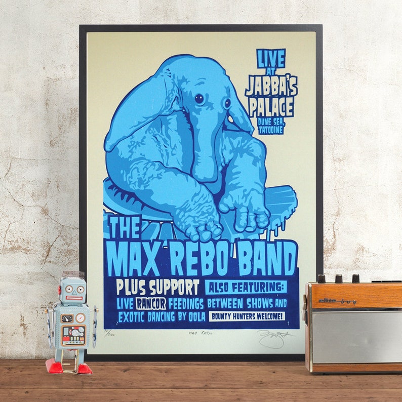 May include: A framed poster featuring a blue elephant-like creature with the text "THE MAX REBO BAND" and "LIVE AT JABBA'S PALACE." The poster includes additional text about the event and is displayed with a vintage robot toy and radio.