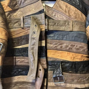 Peut inclure: Veste en cuir vintage avec un design patchwork. La veste présente une variété de bandes de cuir aux tons terre, notamment des nuances de marron, de beige et de noir. Elle a une taille ceinturée et un col classique. C'est une pièce de vêtement unique.