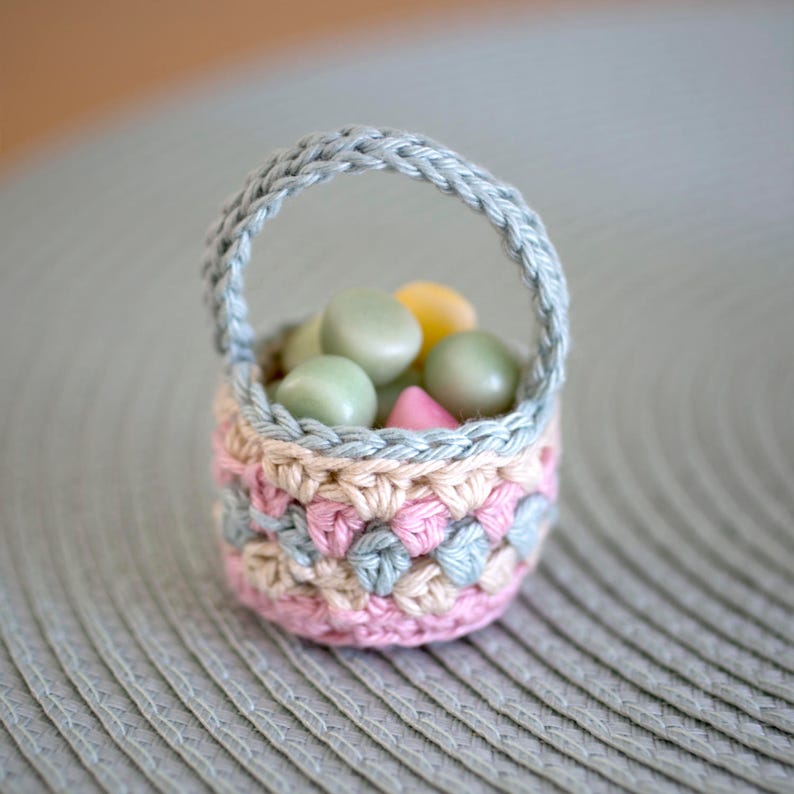 A small crochet basket in light green, yellow and pink filled with small candy of the same colours.
