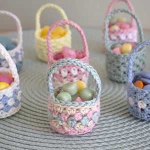 Small crochet baskets on a light green background. The baskets are filled with small candy of different colours.