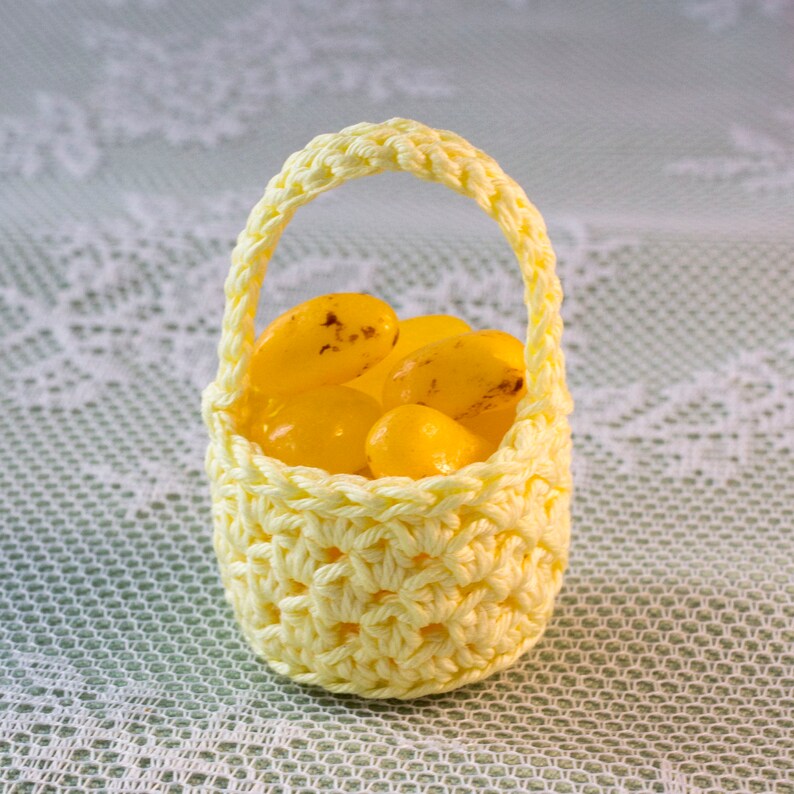 A small crochet basket in yellow is filled with small candy of the same colour.