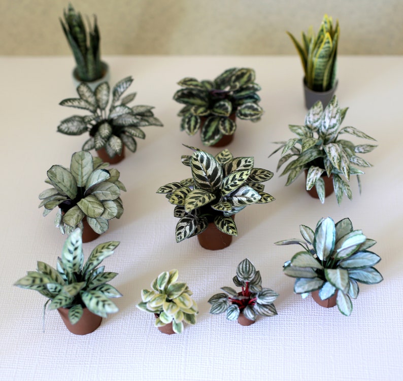 Ten different miniature paper plants are displayed on a floor.