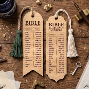 May include: Two wooden Bible bookmarks with tassels. Each bookmark features a list of feelings and corresponding Bible verses. The text "BIBLE EMERGENCY NUMBERS" is printed at the top of each bookmark. One bookmark has a green tassel, the other has a white tassel.