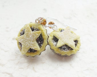 May include: A pair of silver earrings featuring miniature, detailed, edible-looking mince pies with a star-shaped pastry top and a dusting of powdered sugar.