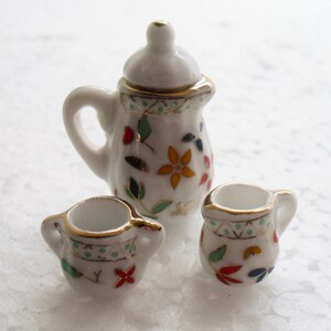 May include: A white porcelain tea set with a floral design. The set includes a teapot, a creamer, and a sugar bowl.