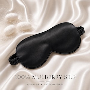 May include: A black mulberry silk sleep mask with an elastic band, resting on a white satin surface. The text "100% MULBERRY SILK" is displayed below the mask, with "Natural Silk &bull; Soft & Breathable" underneath.