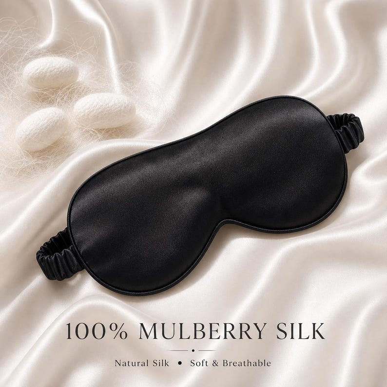 May include: A black mulberry silk sleep mask with an elastic band, resting on a white satin surface. The text "100% MULBERRY SILK" is displayed below the mask, with "Natural Silk &bull; Soft & Breathable" underneath.