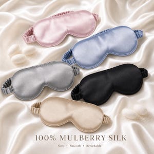 May include: Five silk sleep masks in pink, blue, silver, black, and beige, with elastic bands. The masks are arranged on a white satin surface. Text at the bottom reads "100% Mulberry Silk" with the words "Soft, Smooth, Breathable".