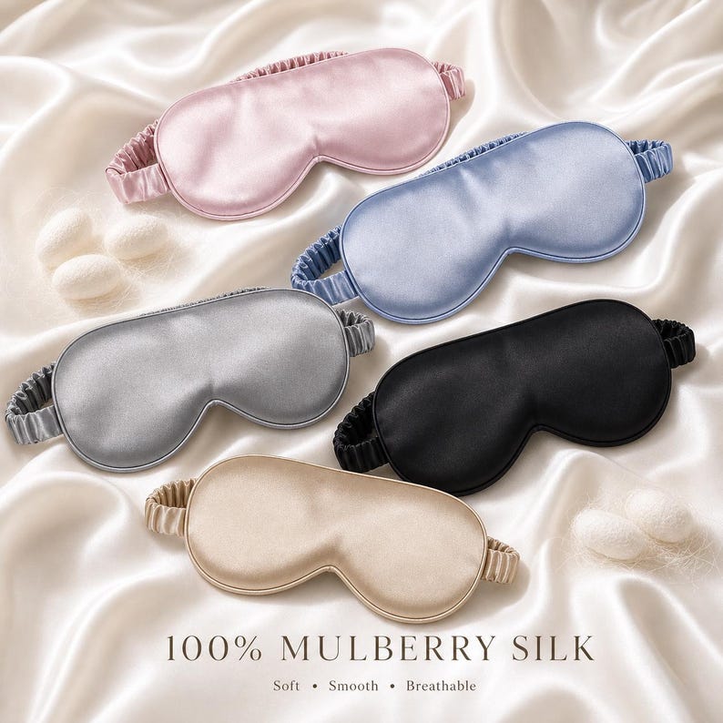 May include: Five silk sleep masks in pink, blue, silver, black, and beige, with elastic bands. The masks are arranged on a white satin surface. Text at the bottom reads "100% Mulberry Silk" with the words "Soft, Smooth, Breathable".