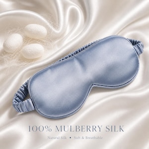 May include: A light blue silk sleep mask with an elastic band, resting on a white satin surface. The text "100% MULBERRY SILK" is displayed below the mask, along with "Natural Silk &bull; Soft & Breathable". Three white cocoons are in the background.