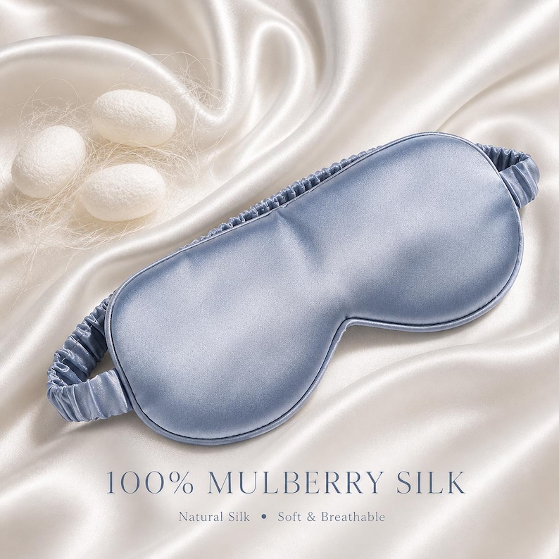 May include: A light blue silk sleep mask with an elastic band, resting on a white satin surface. The text "100% MULBERRY SILK" is displayed below the mask, along with "Natural Silk &bull; Soft & Breathable". Three white cocoons are in the background.