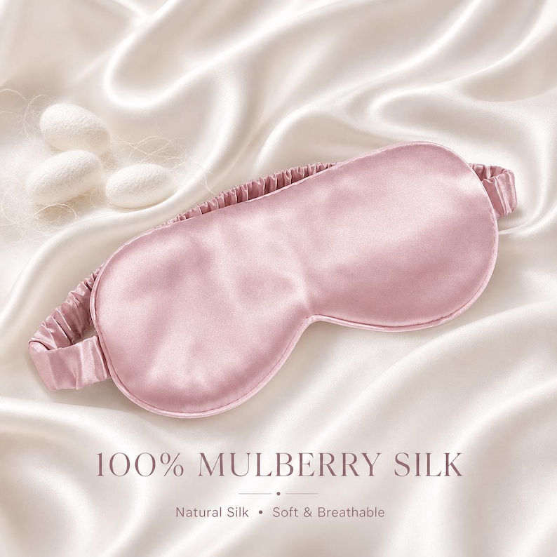 May include: A light pink mulberry silk sleep mask with an elastic band, resting on a white satin surface. The text "100% MULBERRY SILK" is displayed below the mask, with "Natural Silk &bull; Soft & Breathable" underneath.