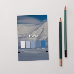Peut inclure: Une carte de palette de couleurs "Arctique" avec une scène de montagne enneigée et une série d'échantillons de couleurs bleues. Deux crayons, un vert et un bleu sarcelle, sont positionnés à droite de la carte.