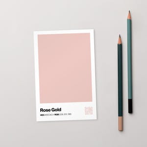May include: A rectangular card with a rose gold color swatch, labeled "Rose Gold" with color code information. Two pencils, one teal and one dark green, are positioned to the right of the card.