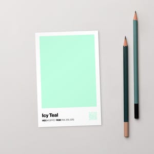 以下が含まれることがあります： 「Icy Teal」のテキストと色の仕様が記載された白い長方形のカードと、2本の鉛筆。カードには、鮮やかなアイスティール色が表示されています。1本の鉛筆は濃いティール色で、もう1本は明るいティール色です。