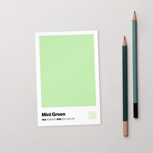 Pode incluir: Uma amostra de cor verde menta com o texto "Mint Green", código HEX e valores RGB. Dois lápis, um verde escuro e outro verde-azulado, estão posicionados à direita da amostra. Os lápis têm um corpo de madeira e uma ponta de grafite.