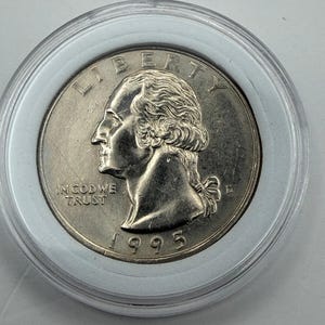 May include: A 1995 United States quarter dollar coin encased in a clear protective plastic capsule. The obverse side features the profile of George Washington facing left, with the text LIBERTY, IN GOD WE TRUST, the year 1995, and the mint mark D.