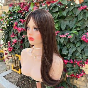 May include: A mannequin head with long, straight brown hair with blonde highlights. The mannequin has full makeup, including red lipstick and eye makeup with glitter accents. It is wearing a pearl necklace and a gold chain necklace with charms.