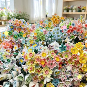 May include: A large collection of small, multi-colored ceramic flowers in shades of pink, yellow, blue, green, and white. Each flower features delicate petals and a central stamen, attached to thin green wire stems, creating a dense floral arrangement.