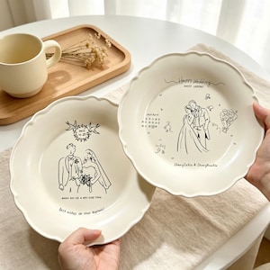May include: Two cream-colored ceramic plates with scalloped edges, each featuring black line-art illustrations of a wedding couple. One plate displays the text "Best wishes on your Nuptials!" and the other "Happy Wedding SWEET EVERYDAY".