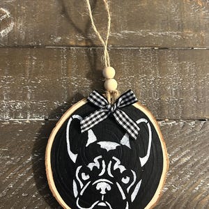 May include: A round, wooden ornament featuring a black background with a white French Bulldog design. The ornament has a natural wood edge, a black and white checkered bow, and a twine loop for hanging.