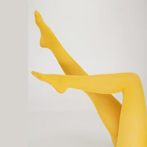 May include: Two legs in bright yellow tights are crossed against a white background. The tights are opaque and smooth, with a solid color. The legs are positioned at an angle, creating a dynamic and eye-catching composition.