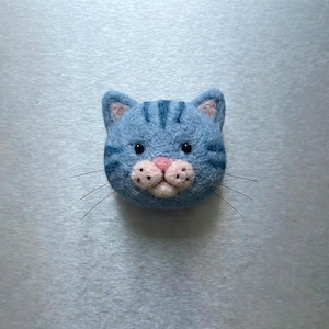 Pu&ograve; includere: Testa di gatto in feltro blu con strisce blu scuro, interno orecchie rosa e naso rosa. Il gatto ha occhi neri e lunghi baffi neri. &Egrave; un oggetto fatto a mano.