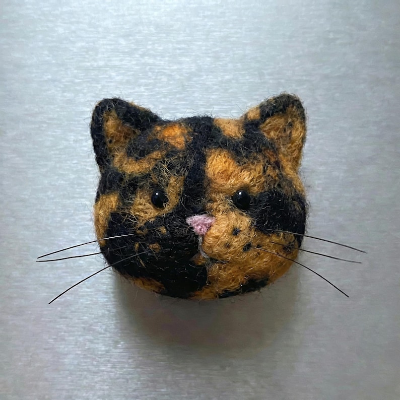 Pu&ograve; includere: Spilla fatta a mano a forma di testa di gatto, con un motivo a scaglie di tartaruga nero e arancione. Il gatto ha un naso rosa, occhi neri e baffi di filo. Accessorio unico.