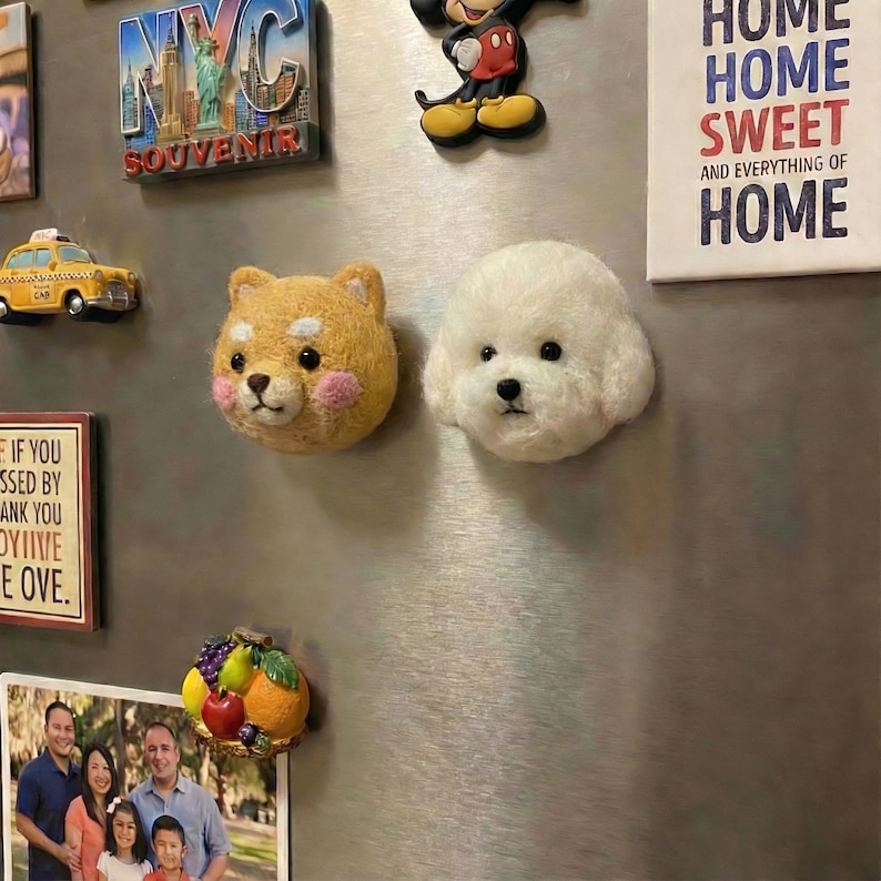 May include: A collection of decorative magnets on a refrigerator. The magnets include a yellow taxi cab, a Shiba Inu dog head, a white Bichon Frise dog head, a Mickey Mouse figure, and a NYC souvenir. A sign reads "HOME SWEET HOME".