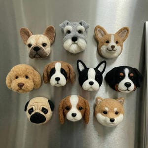 Könnte beinhalten: Eine Sammlung handgefertigter Filz-Hunde-Kopfmagnete, darunter Französische Bulldoggen, Schnauzer und Corgis. Jeder Magnet zeigt detaillierte Gesichtszüge und realistische Farben. Ideal zur Dekoration von Kühlschränken oder anderen magnetischen Oberflächen.