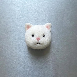 Pu&ograve; includere: Una testa di gatto in feltro bianco con l'interno delle orecchie e il naso rosa. Il gatto ha occhi neri e sottili baffi. Questo oggetto decorativo fatto a mano rappresenta un volto di gatto.
