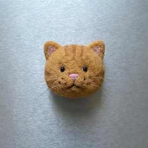 Pu&ograve; includere: Testa di gatto arancione fatta a mano in feltro. Il gatto ha occhi neri, naso rosa e baffi. Le orecchie sono foderate di feltro rosa. Questo oggetto a tema gatto &egrave; probabilmente una spilla o un magnete decorativo.