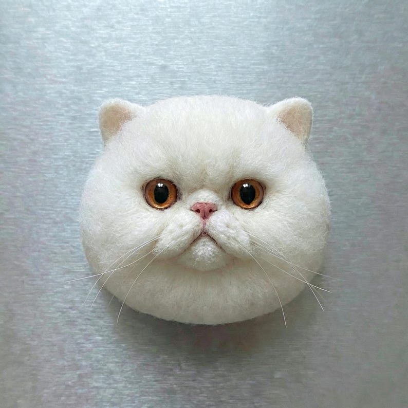 May include: A white, fluffy cat face with large, round, amber-colored eyes and a small pink nose. The cat has a slightly grumpy expression and long, thin whiskers. The cat's face is centered on a light gray background.