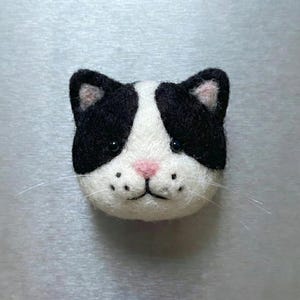 Pu&ograve; includere: Un volto di gatto in feltro fatto a mano con pelo bianco e nero, naso rosa e baffi. Il volto del gatto &egrave; centrato, mostrando i suoi dettagli e la sua maestria artigianale. Un affascinante oggetto decorativo.