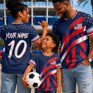May include: Three matching navy blue V-neck jerseys featuring a red and white diagonal stripe pattern, white stars on the shoulders, and a small American flag graphic. One jersey displays the text YOUR NAME and the number 10 on the back.